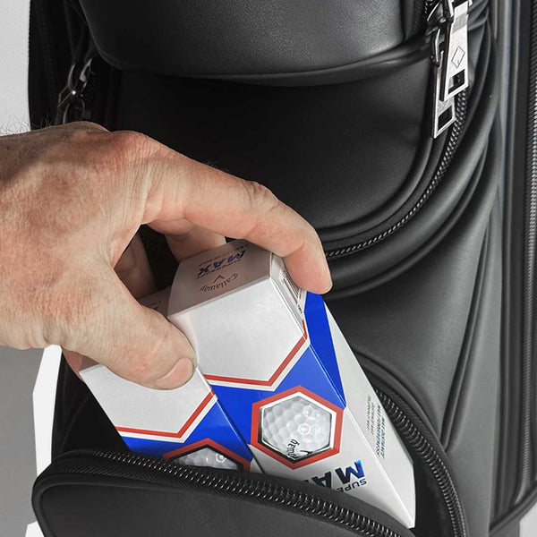 Hand placing a box of golf balls into a black golf bag.