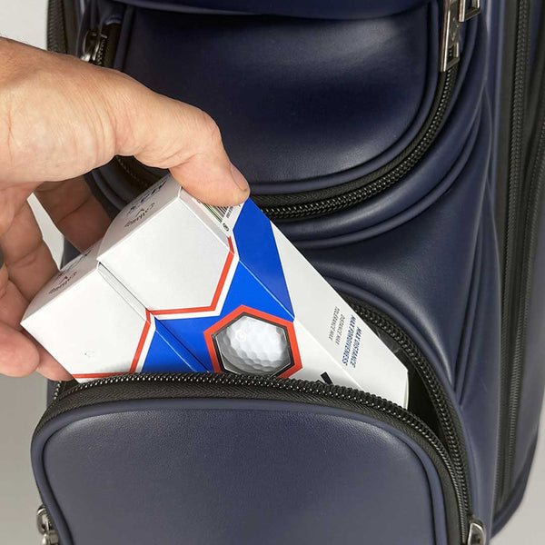 Hand placing a box with a geometric design into a navy golf bag.