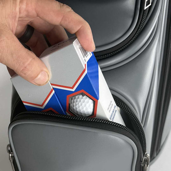 Hand placing a golf ball and club into a gray suitcase.
