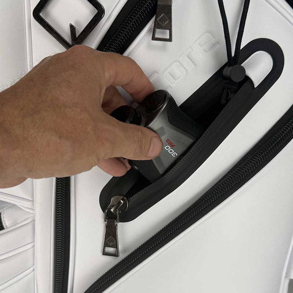 Hand placing a device into a compartment of a white suitcase with black zippers.