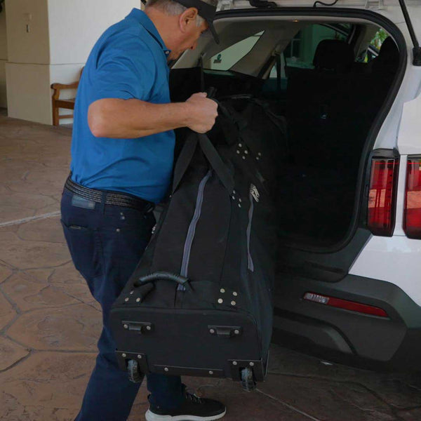 Man loading a large black duffel bag into the trunk of a white car.