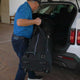 Man loading a large black duffel bag into the trunk of a white car.