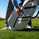 Person reaching into a white golf bag labeled 'RevCore' on a golf course.