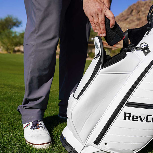 Person opening a white golf bag with 'Rev' branding on a golf course.